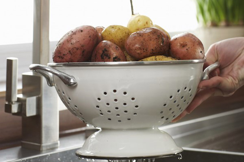 Hands holding potatoes in a colander under the faucet