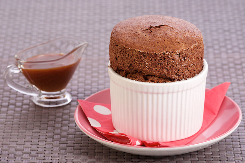 Chocolate souffle in a white ramekin with salted caramel sauce on the side