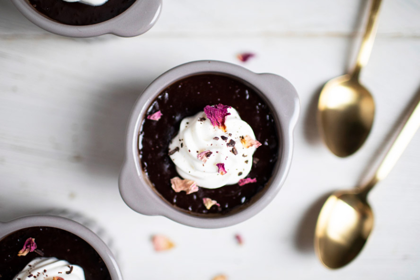Individual chocolate and coconut pots De crème topped with coconut whipped cream and dried rose petals