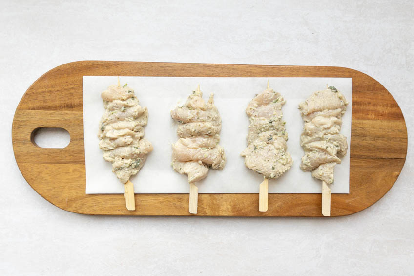 Uncooked chicken skewers on a serving board