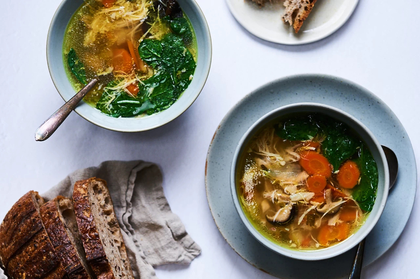 Two bowls of chicken soup with carrots, spinach and mushrooms