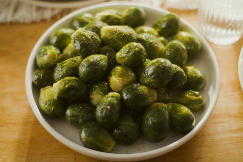 A bowl of steamed Brussels sprouts on a wooden table