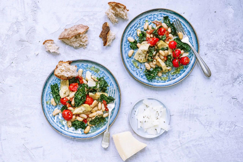 Two blue plates with Tuscan white beans, kale, cherry tomatoes and artichokes