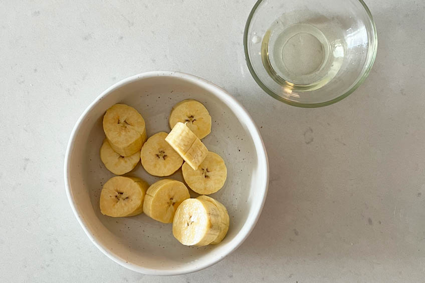 A bowl with plantains cut into small one-inch pieces and a small jar of neutral oil