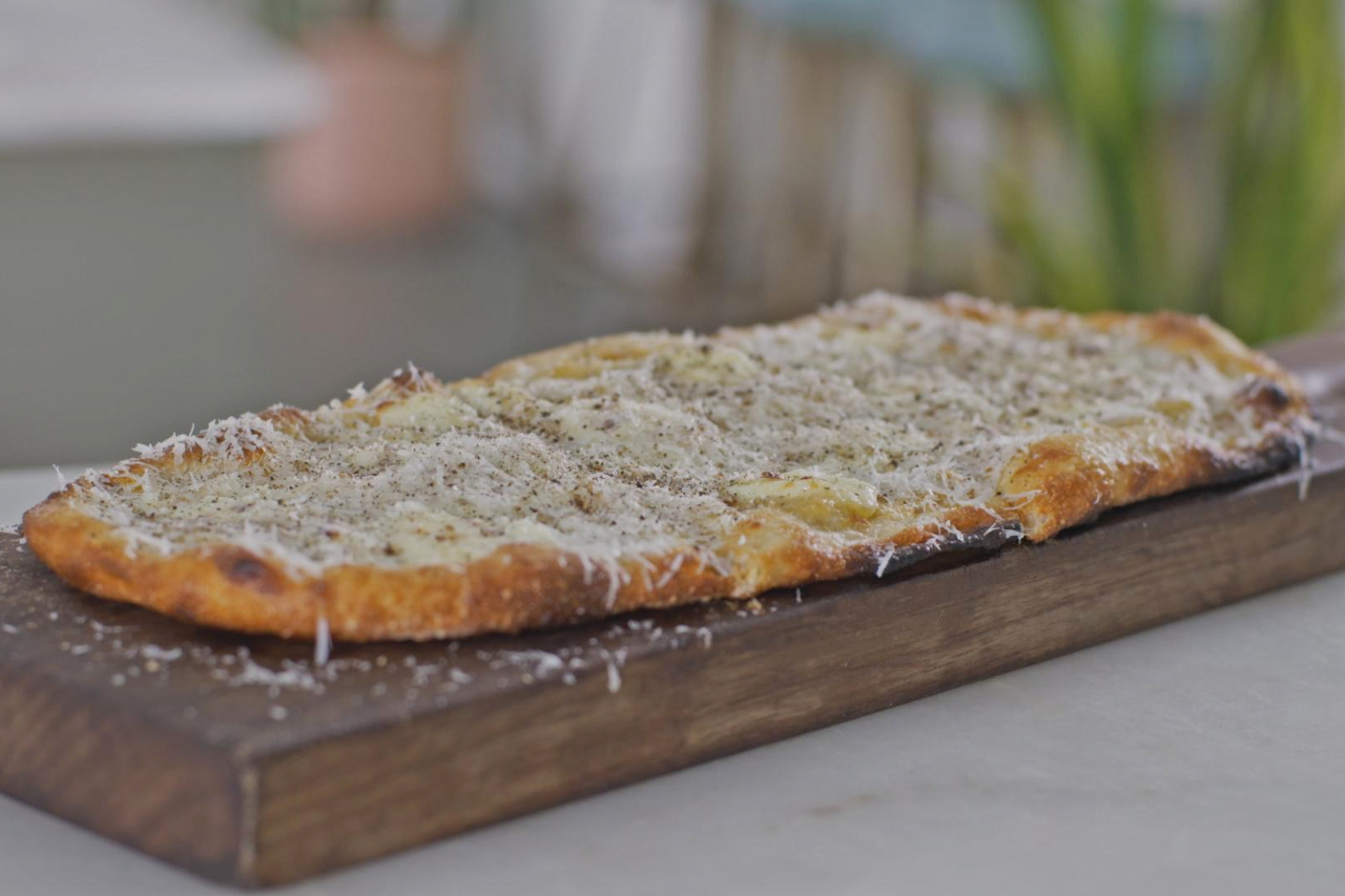 A long cacio e pepe pizza made with cheese and garlic, served on a cutting board