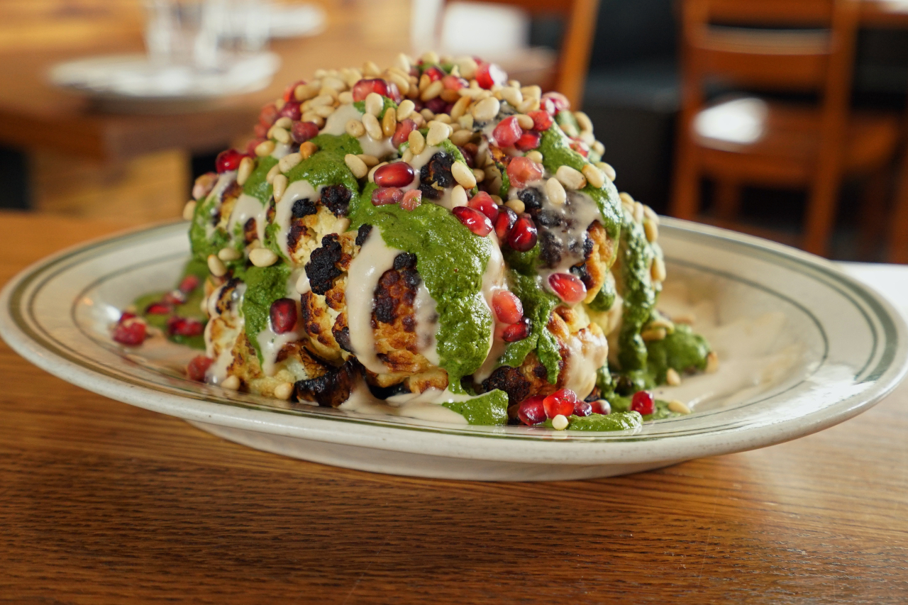 Whole roasted cauliflower stuffed with halloumi and topped with skhug, pine nuts and pomegranate seeds