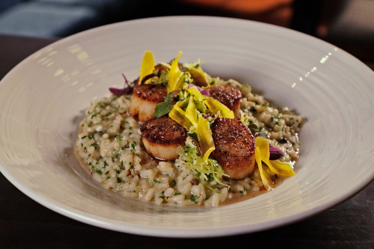 A bowl of risotto topped with seared scallops and shaved, cured egg yolk