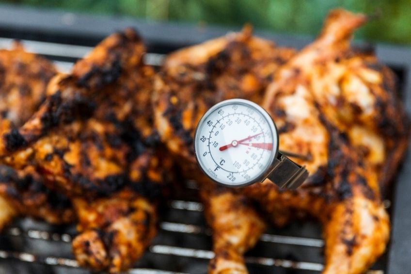 thermometer being inserted into chicken on a grill