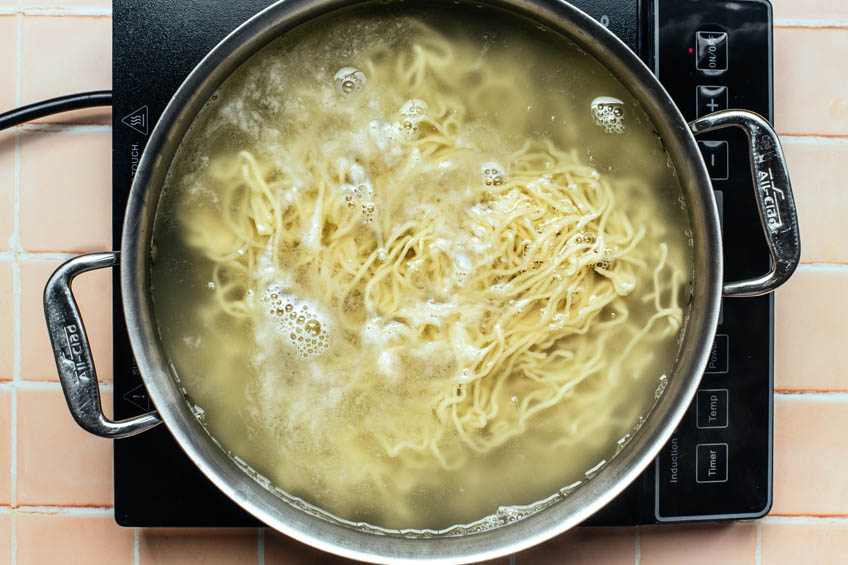Chinese egg white noodles being boiled in a pot
