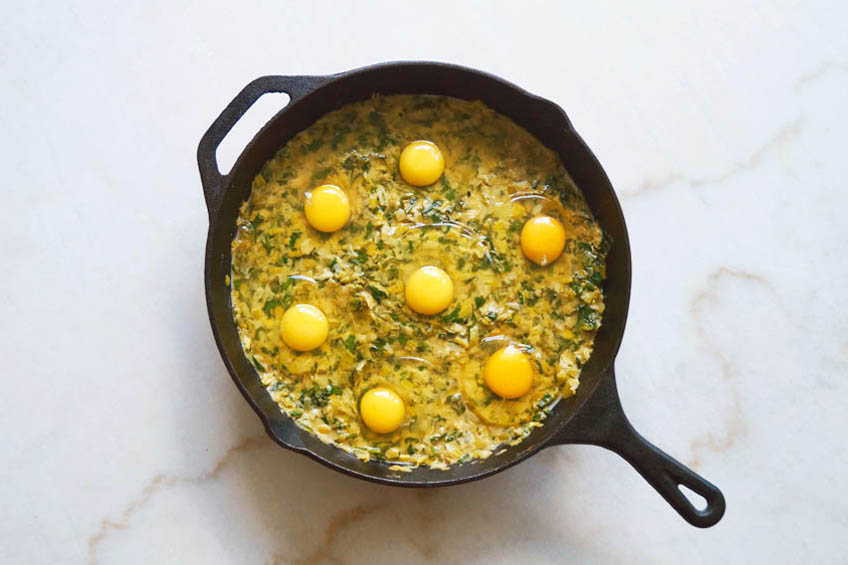 Uncooked eggs on a green base of veggies for creamy leek and spinach shakshuka