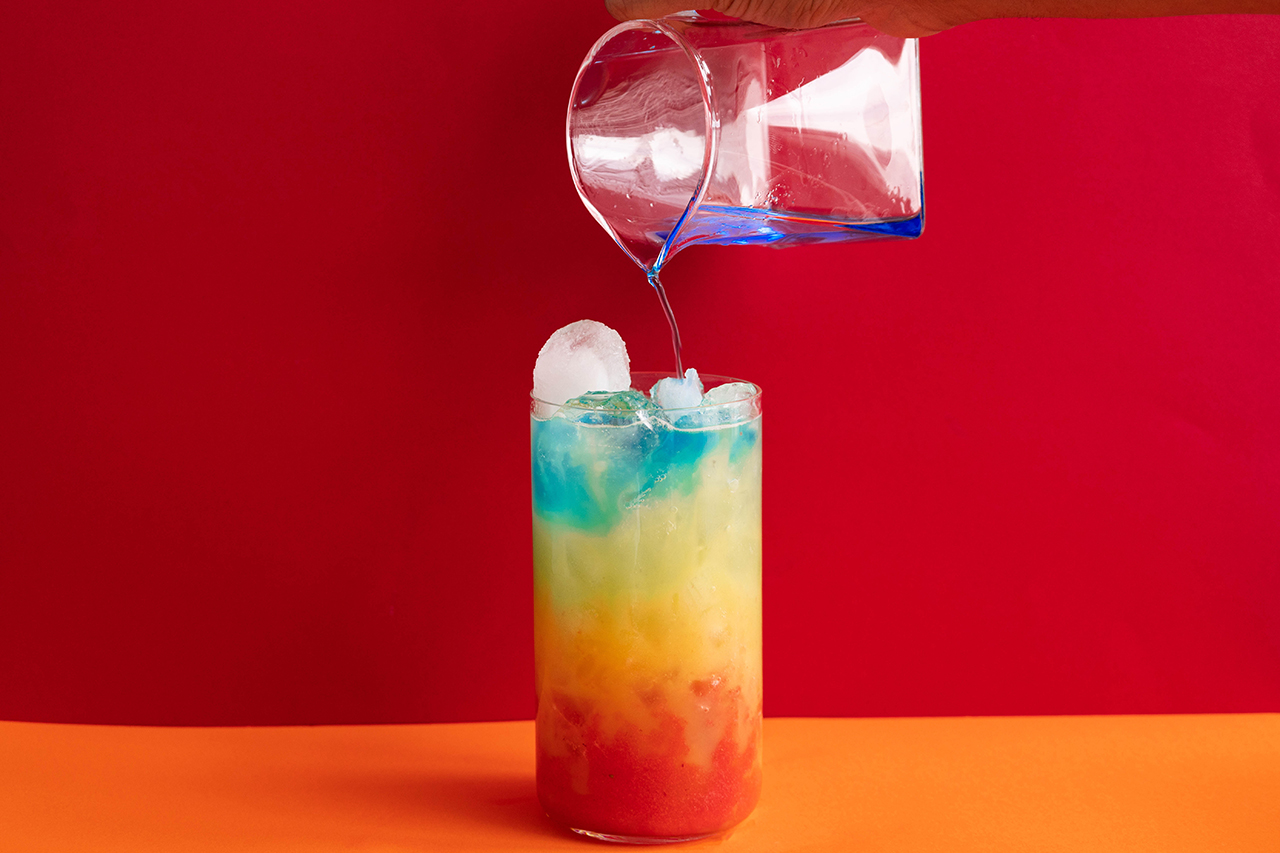 Over the rainbow cocktail with blue curacao being poured