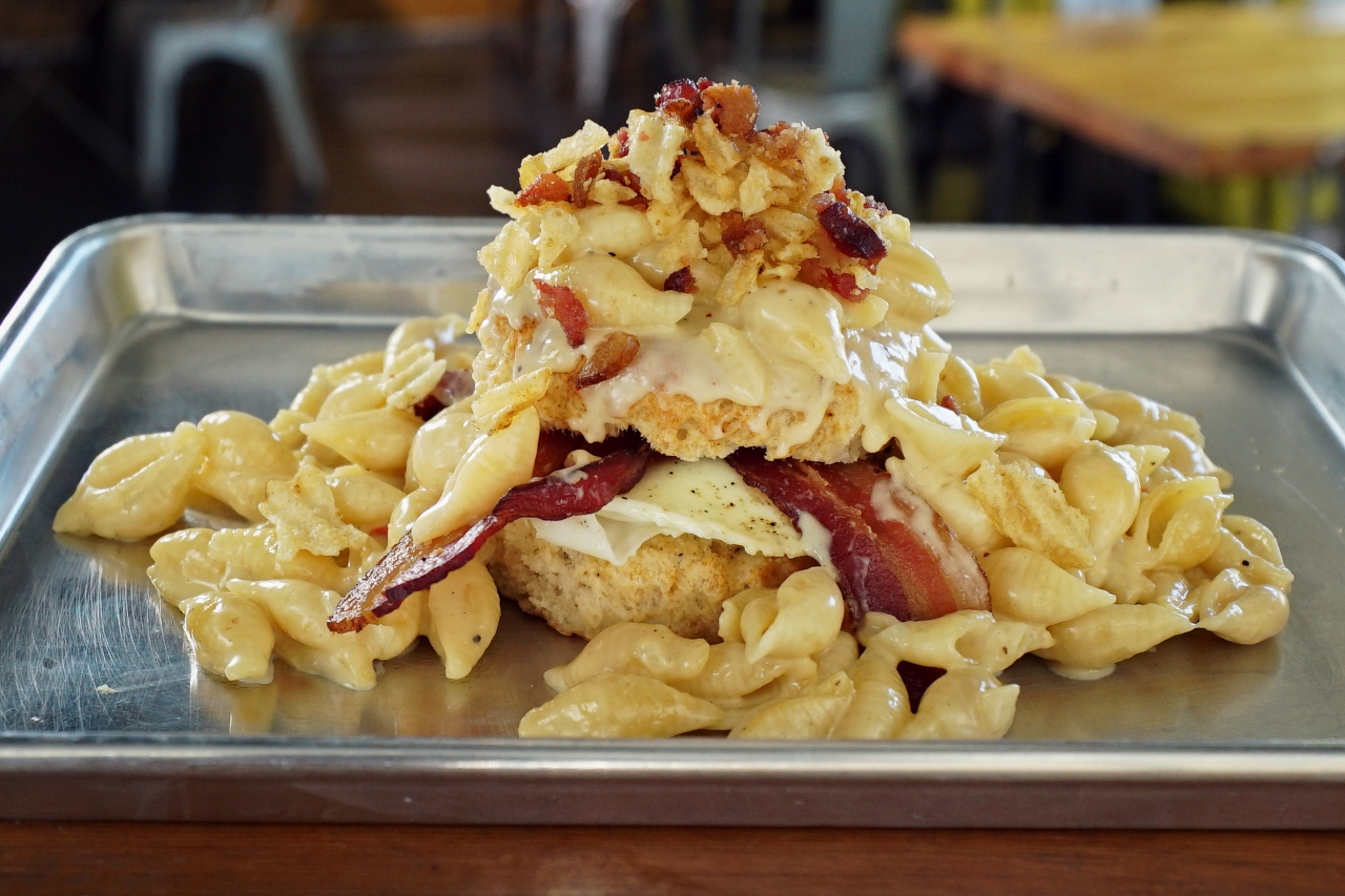 Mac and cheese piled on a metal tray with garlicky toast, bacon and a runny egg
