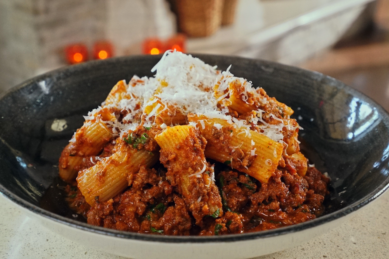 Close-up shot of rigatoni bolognese from Two Sisters Vineyard, sprinkled with a generous handful of cheese