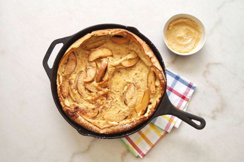 A puffy and golden Dutch baby with apples and honey butter, ready to serve