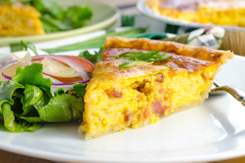A slice of a bacon and egg quiche with a side salad
