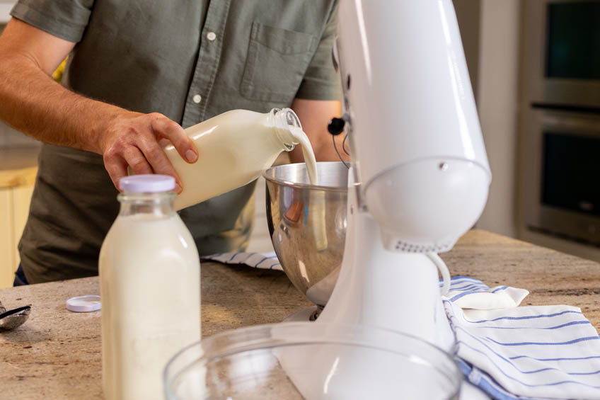 Heavy cream being poured into the bowl of a stand mixer.