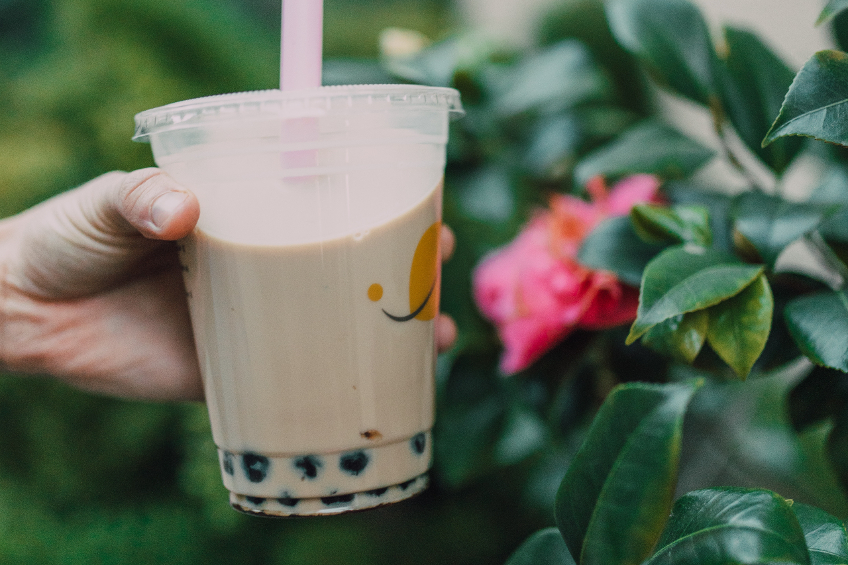 A hand holds a milk tea with pearls up near a rose garden