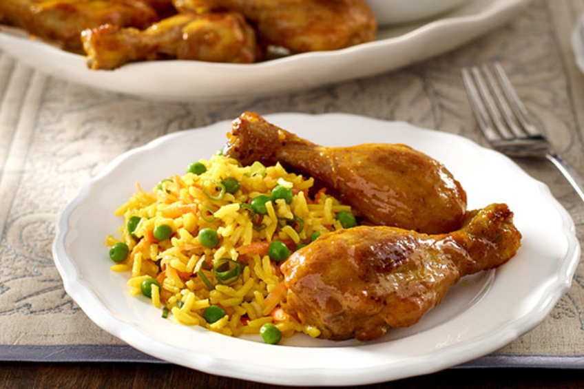 A plate of spiced basmati rice with pies and curry-spiced chicken drumsticks