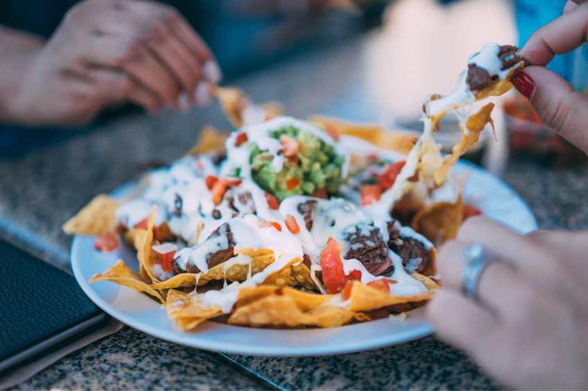 Hands reach for a plate of fully-loaded nachos