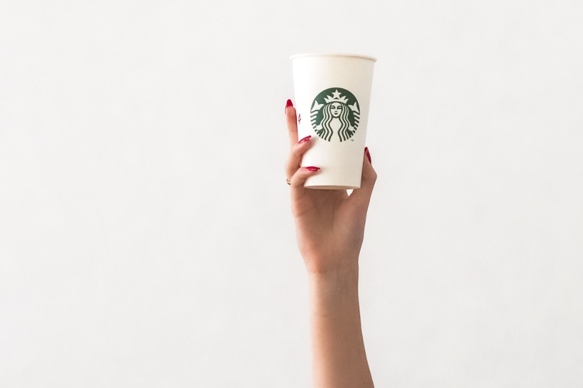 A hand with painted red nails holds up a Starbucks coffee cup