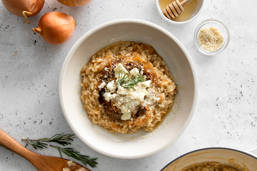 An overhead shot of a caramelized onion risotto with fresh rosemary, parmesan cheese