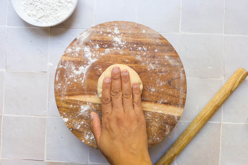 Aloo paratha dough ball being pressed on a cutting board