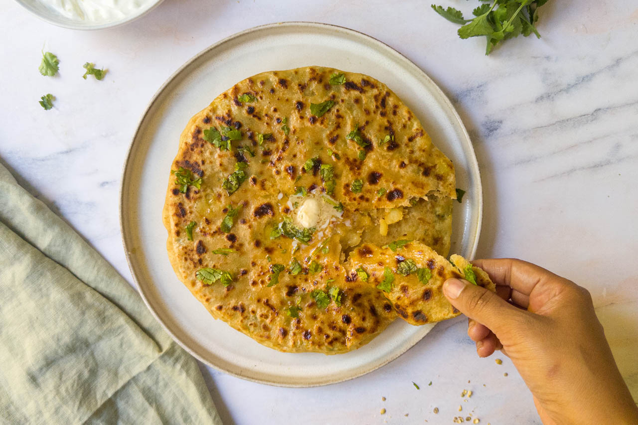 Aloo paratha being torn on a plate