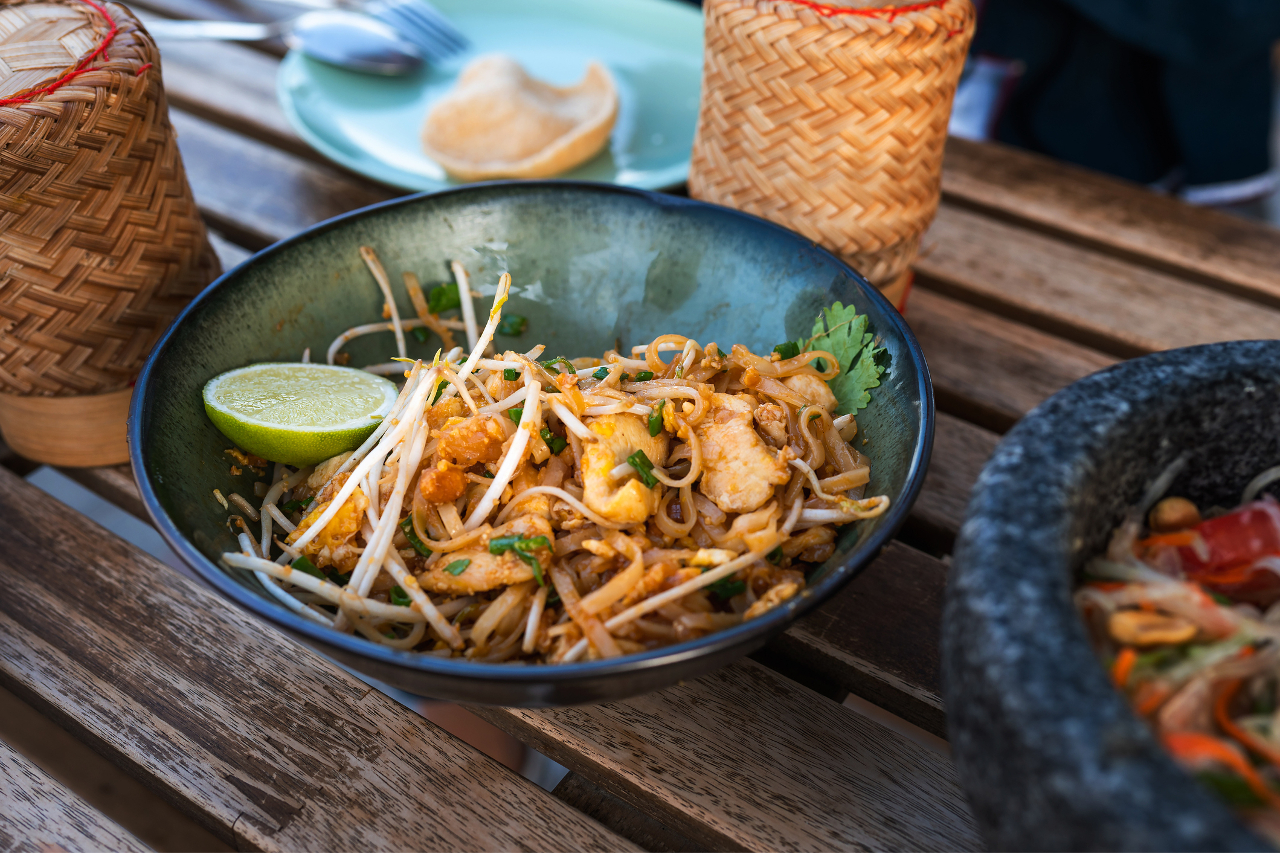 A bowl of pad thai with bean sprouts and a slice of lime to accompany is seen on a table