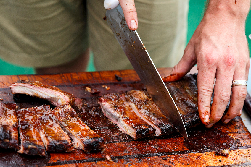 BBQ Ribs being cut on a wooden board