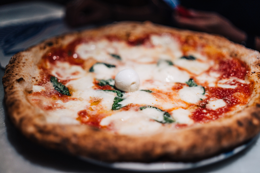 A wood-fired margherita pizza is seen in a close-up