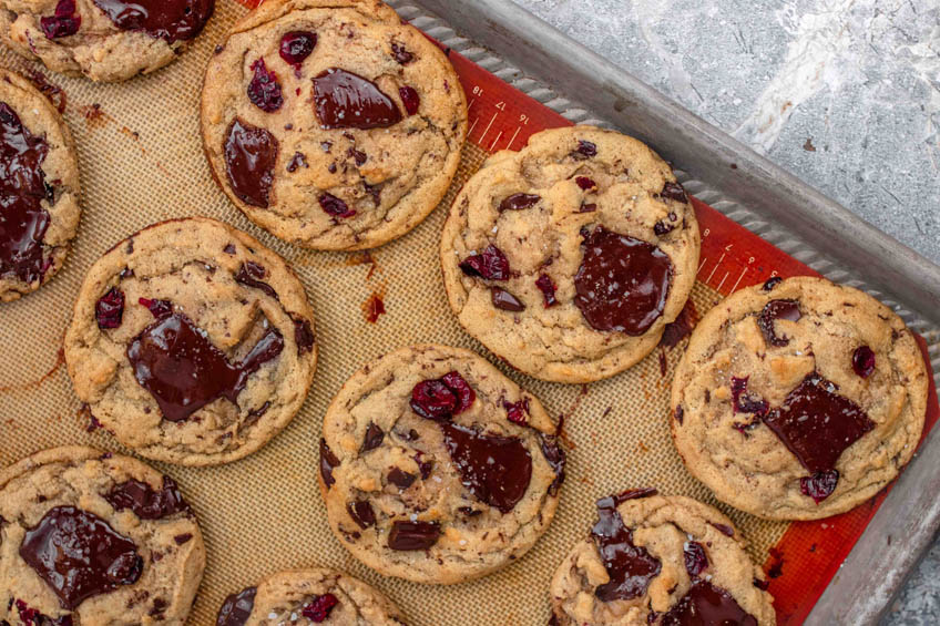 Dark chocolate cranberry cookies fresh out of the oven on a baking sheet.