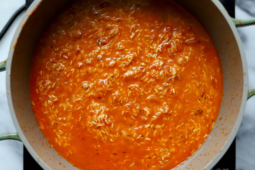 Uncooked rice in tomato stew in a Dutch oven for jollof rice
