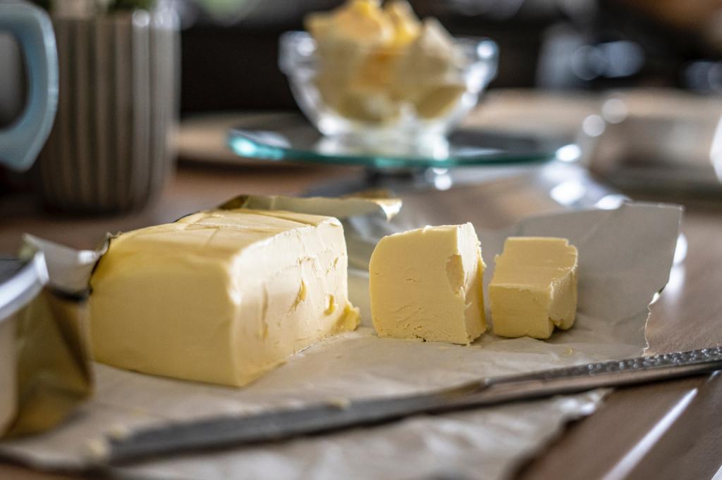 A large stick of butter with some pats cut up beside it and in a bowl in the distance