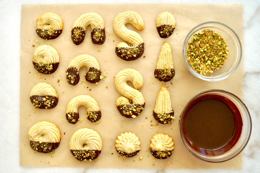 Spritz cookies on parchment paper with pistachios and chocolate