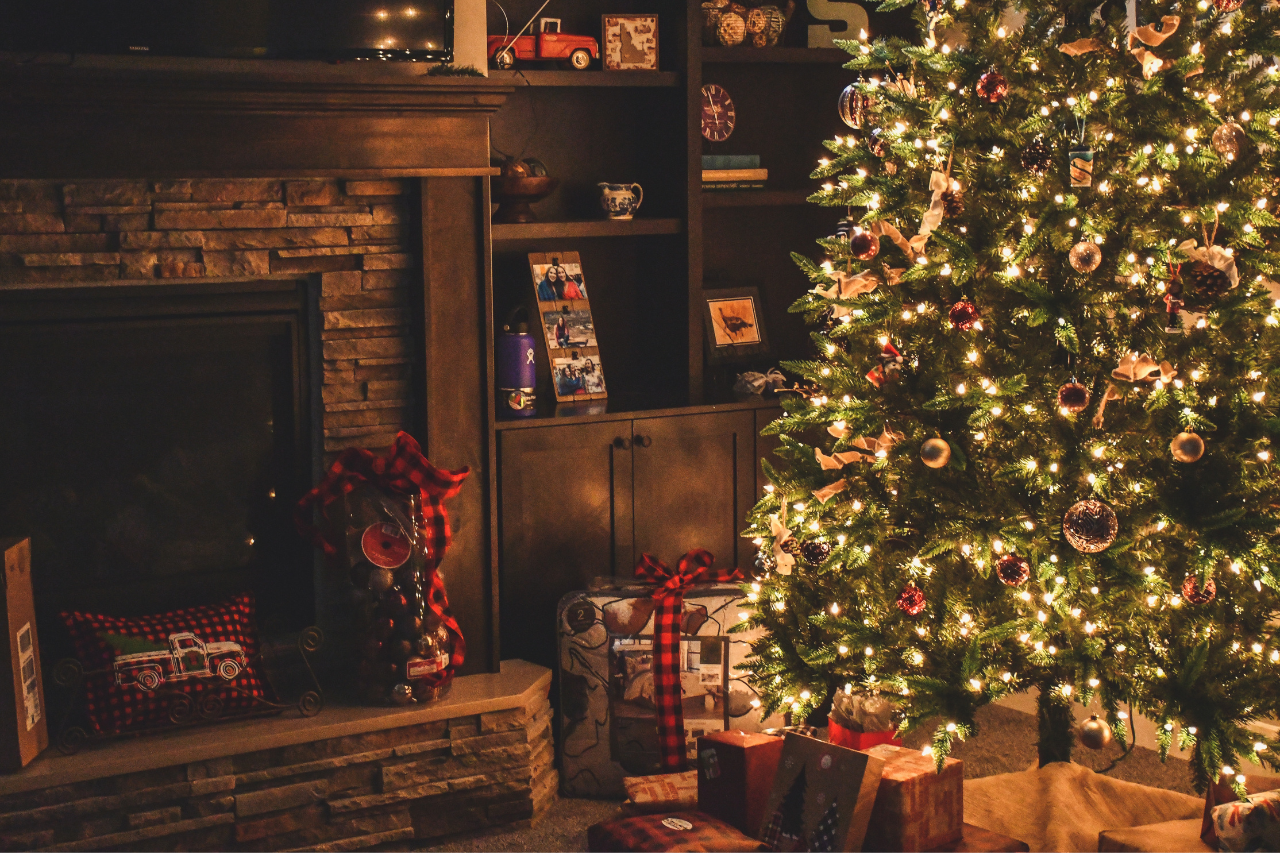 A living room at Christmas time, a lit up tree and gifts around the fireplace