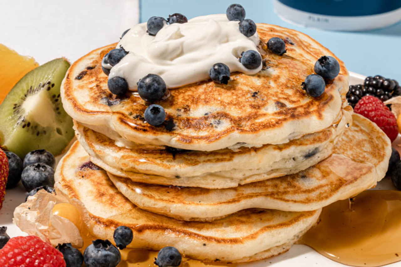 A stack of blueberry pancakes topped with fresh blueberries and yogurt
