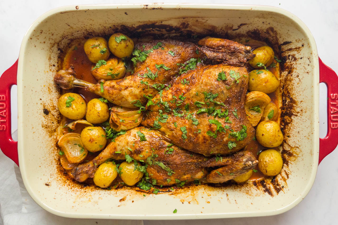Whole roasted tandoori chicken with potatoes in a casserole dish