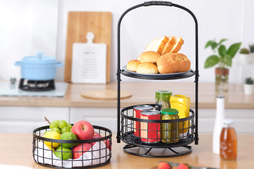 A black wire two-tire rotating kitchen basket filled with various baked goods and fresh produce