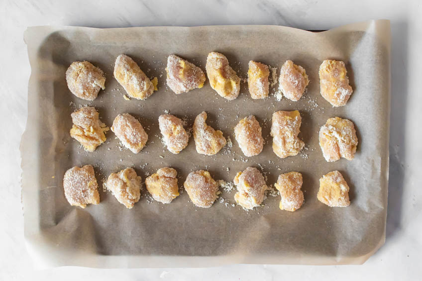 Uncooked breaded chicken bites in a parchment-lined baking sheet