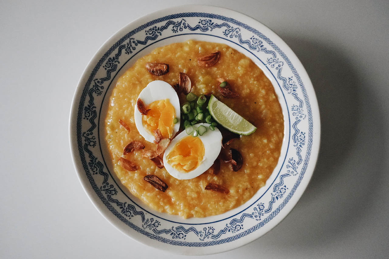 A bowl of lugaw (Filipino rice porridge) topped with a hard boiled eggs, crispy garlic, lime and scallions