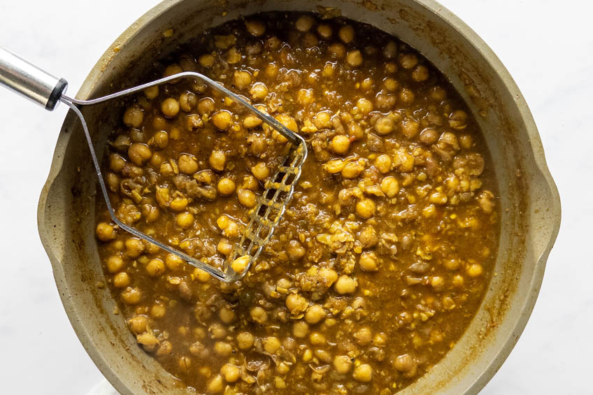 Punjabi chole being mashed in a saute pan with a potato masher
