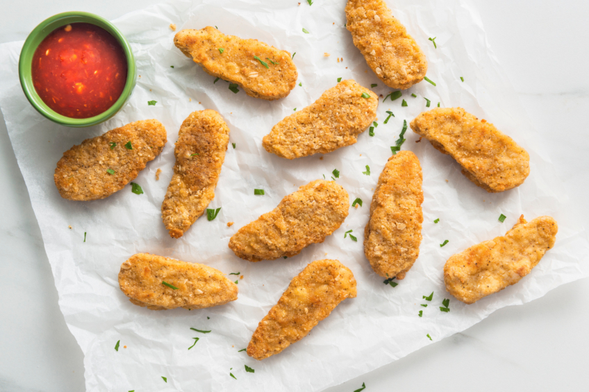 Plant-based chicken tenders on parchment paper with a side dipping sauce