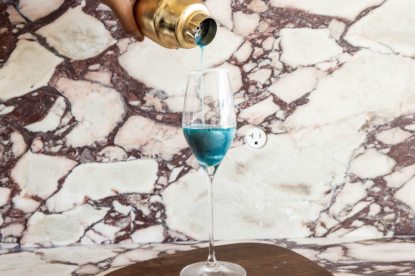 Glittery blue lagoon cocktail being strained into a champagne flute