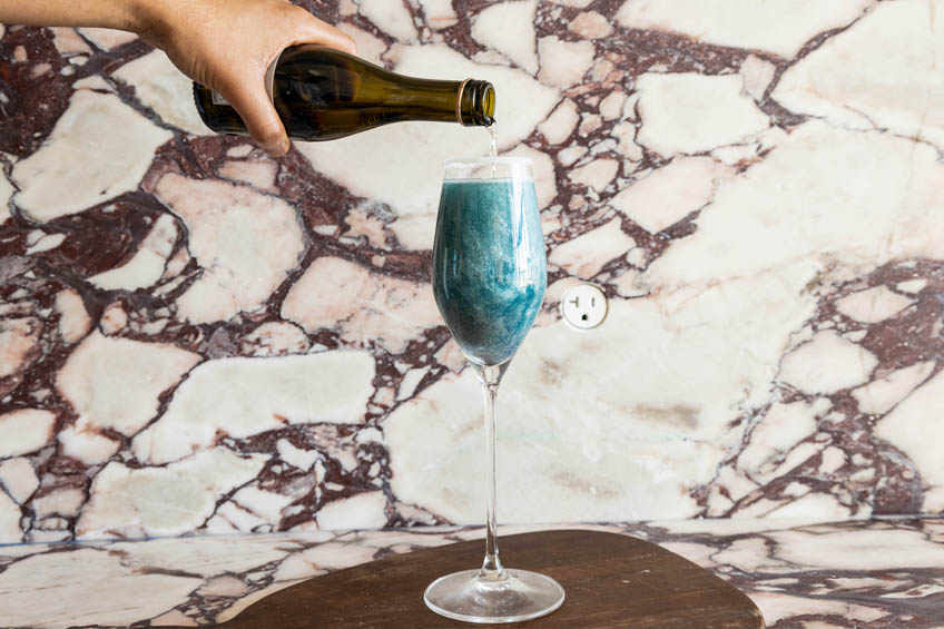 Glittery blue lagoon cocktail being topped with prosecco