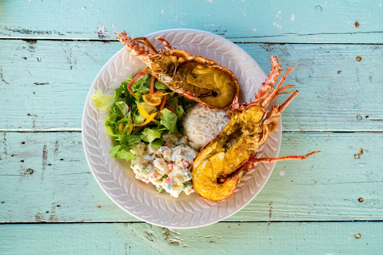 A bowl with rice, two types of salad and a boiled lobster