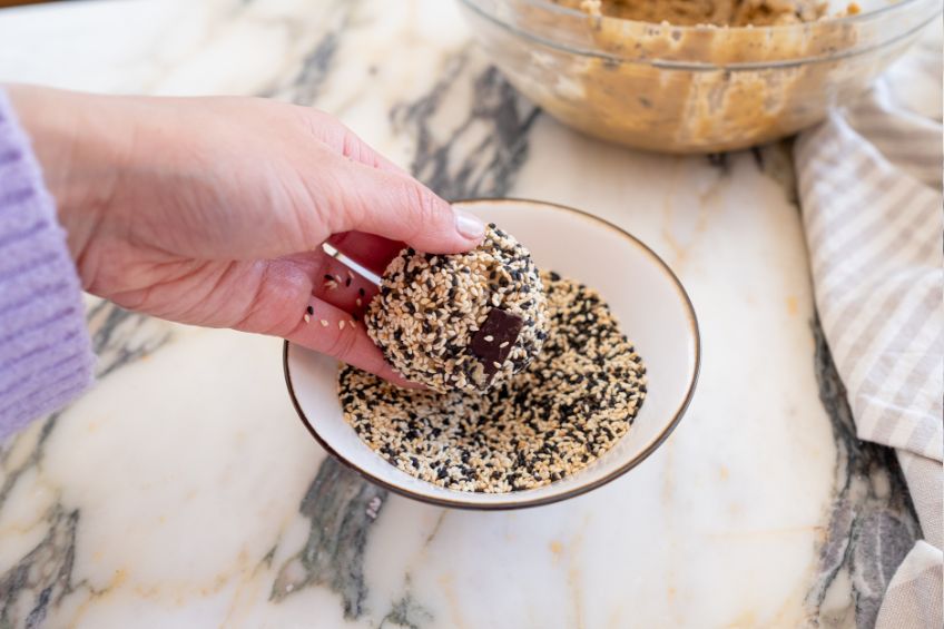A ball of chocolate tahini cookie dough being rolled in sesame seeds