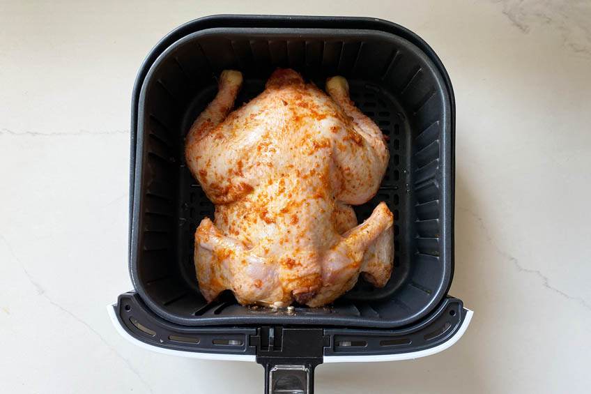 A chicken laid breast-down in an air fryer basket