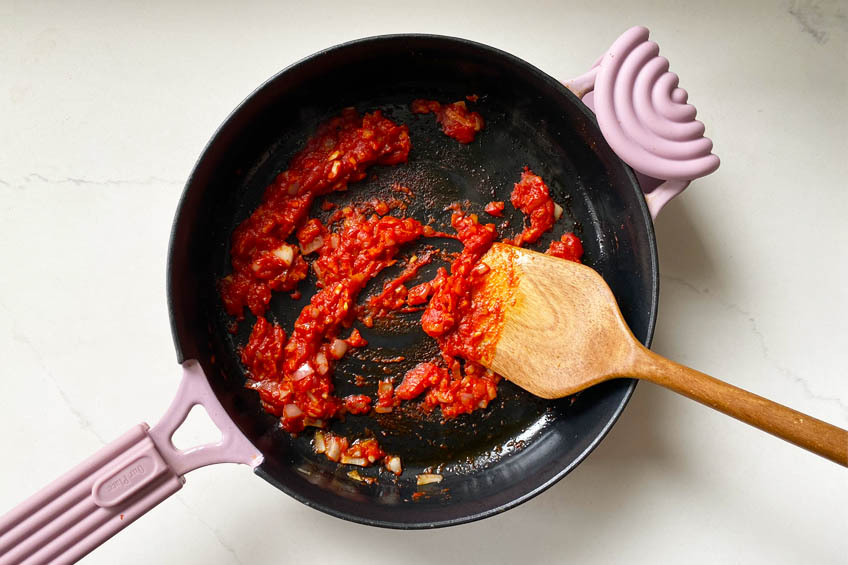 Tomato paste frying with olive oil, shallots and garlic in a skillet.
