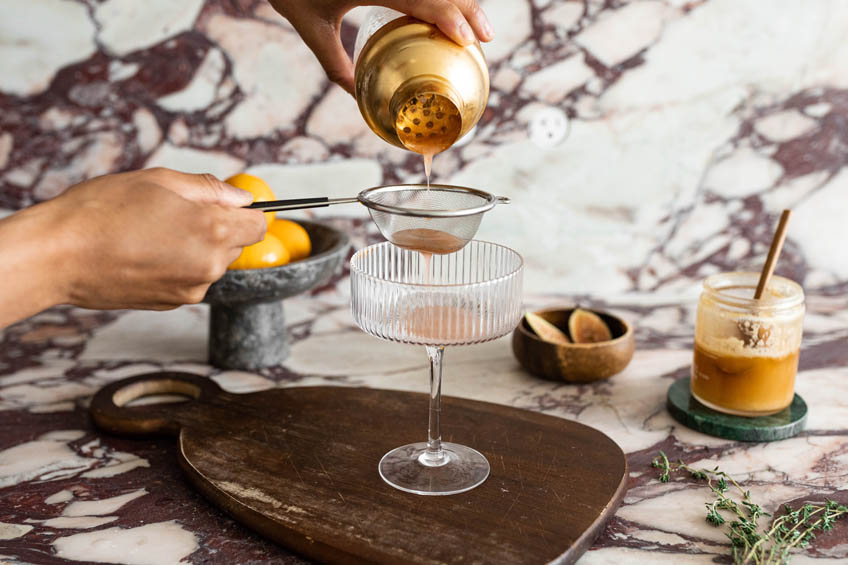 Beyonce-inspired Pure/Honey cocktail being strained into a cocktail coupe