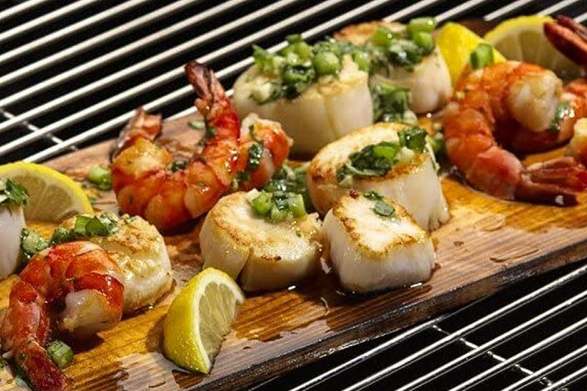 A cedar plank on a grill with shrimp and scallops
